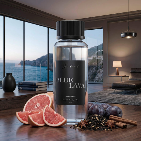 Scentiment Blue Lava diffuser fragrance oil bottle with grapefruit slices, plums and spices on a wooden surface in an executive-style room with large windows overlooking the ocean coast.