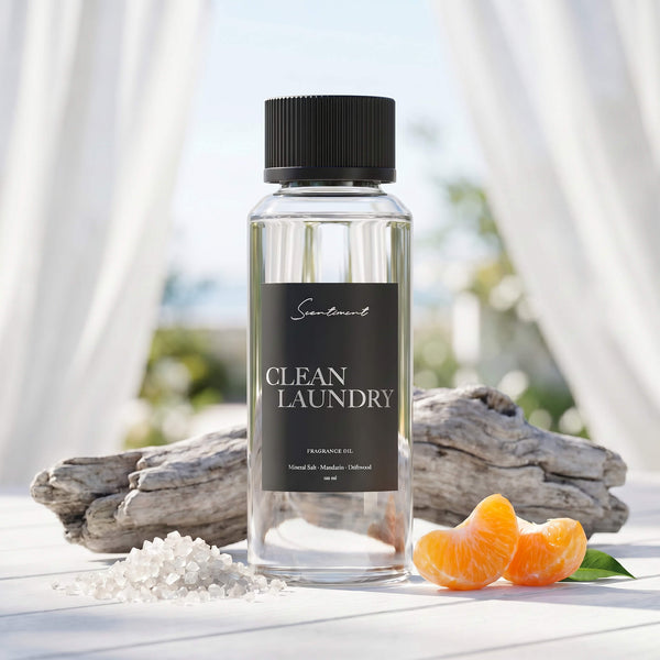 Scentiment Clean Laundry diffuser fragrance oil  bottle on a white wooden surface with oranges and driftwood with linen drapes overlooking a scenic background.