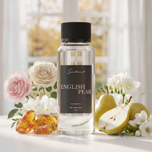 Scentiment English Pear diffuser fragrance oil surrounded with green pears, roses, and amber stones on a white surface with a window covered in linen drapes in the background.